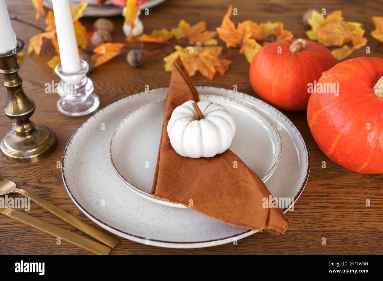 Tavolo festivo per l'autunno, l'autunno, Halloween o il giorno del Ringraziamento. Foglie cadute, zucche e tovagliolo sul piatto su sfondo di legno. Foto Stock