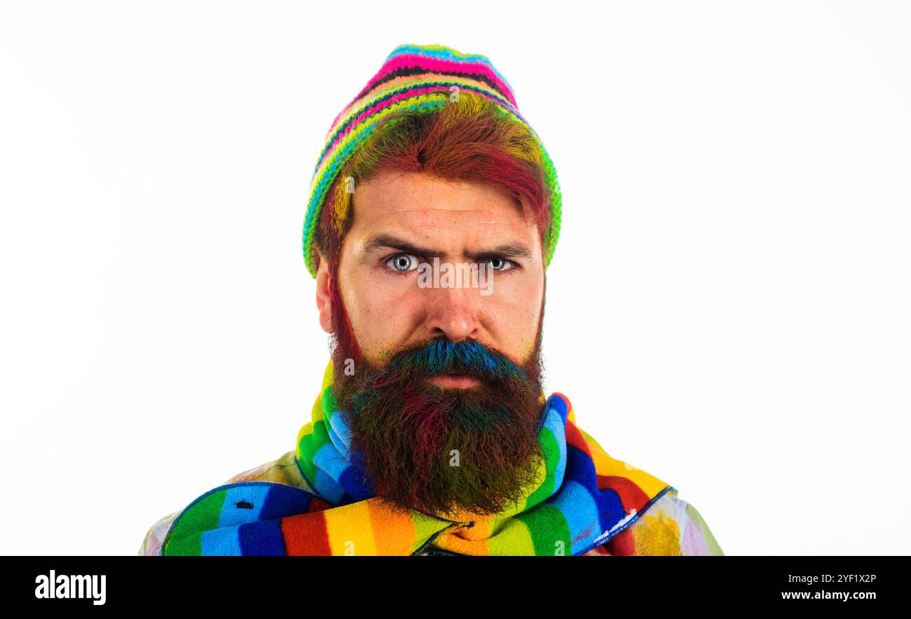Ritratto di un uomo serio ed elegante con barba e capelli tinti con cappello e sciarpa colorati. Bel ragazzo alla moda in un elegante cappello a maglia e a righe Foto Stock