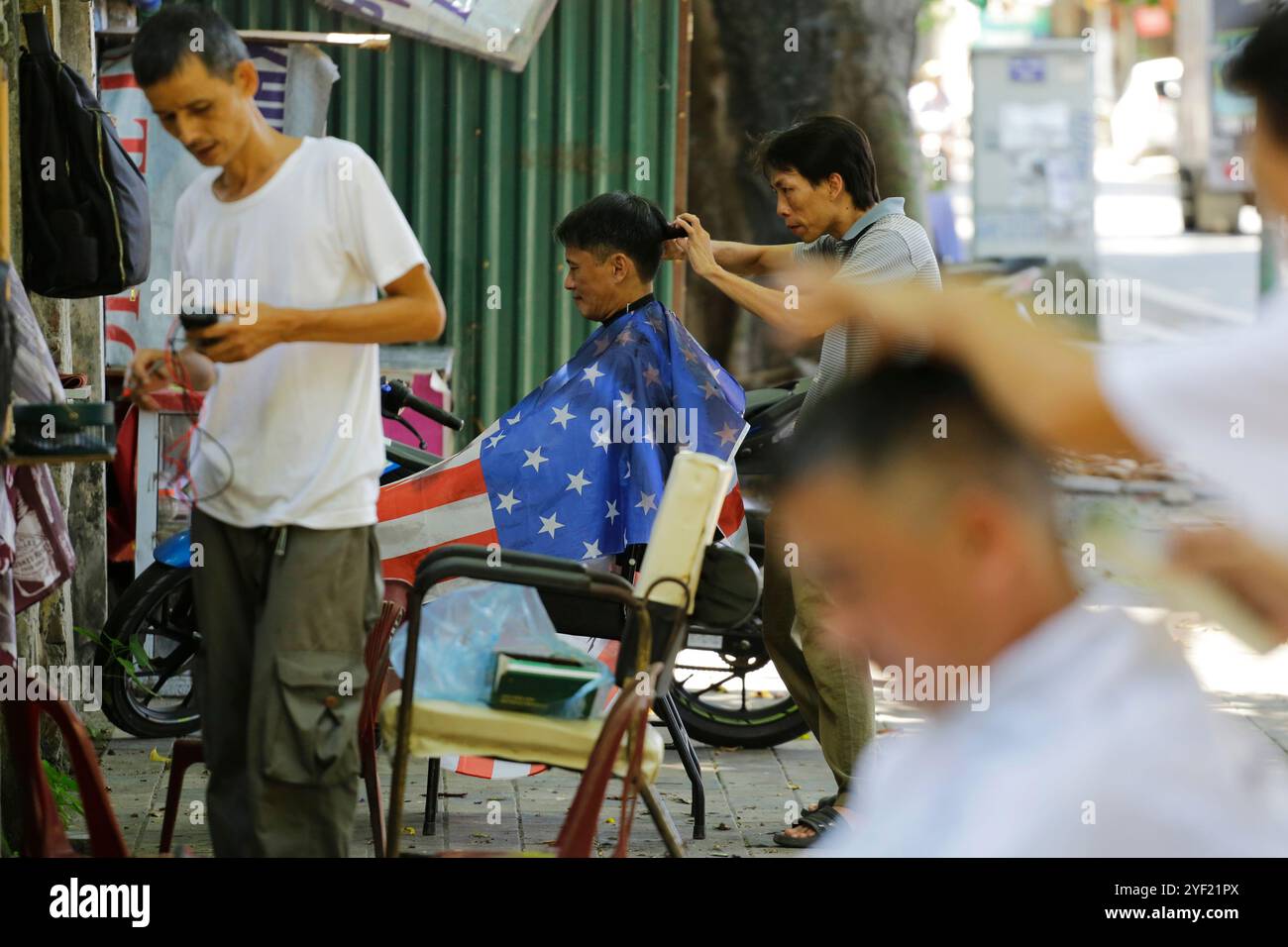 Hanoi, Vietnam - 22 luglio 2023: I barbieri tagliano i capelli dei clienti in un parrucchiere sul marciapiede. Foto Stock