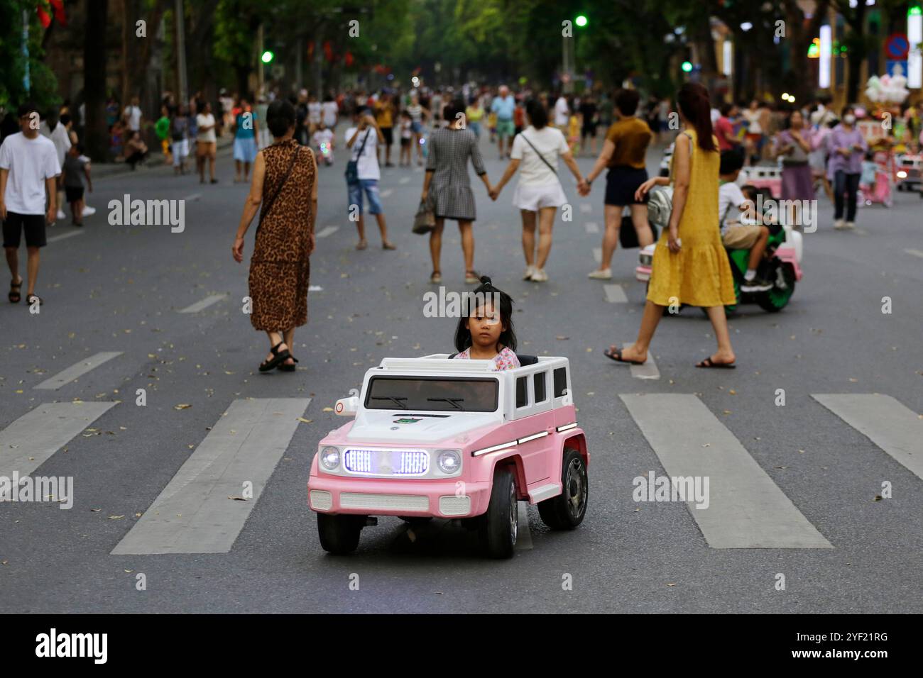 Hanoi, Vietnam - 16 luglio 2023: Una bambina cavalca un'auto giocattolo elettrica in una strada aperta vicino al lago Hoan Kiem. Foto Stock