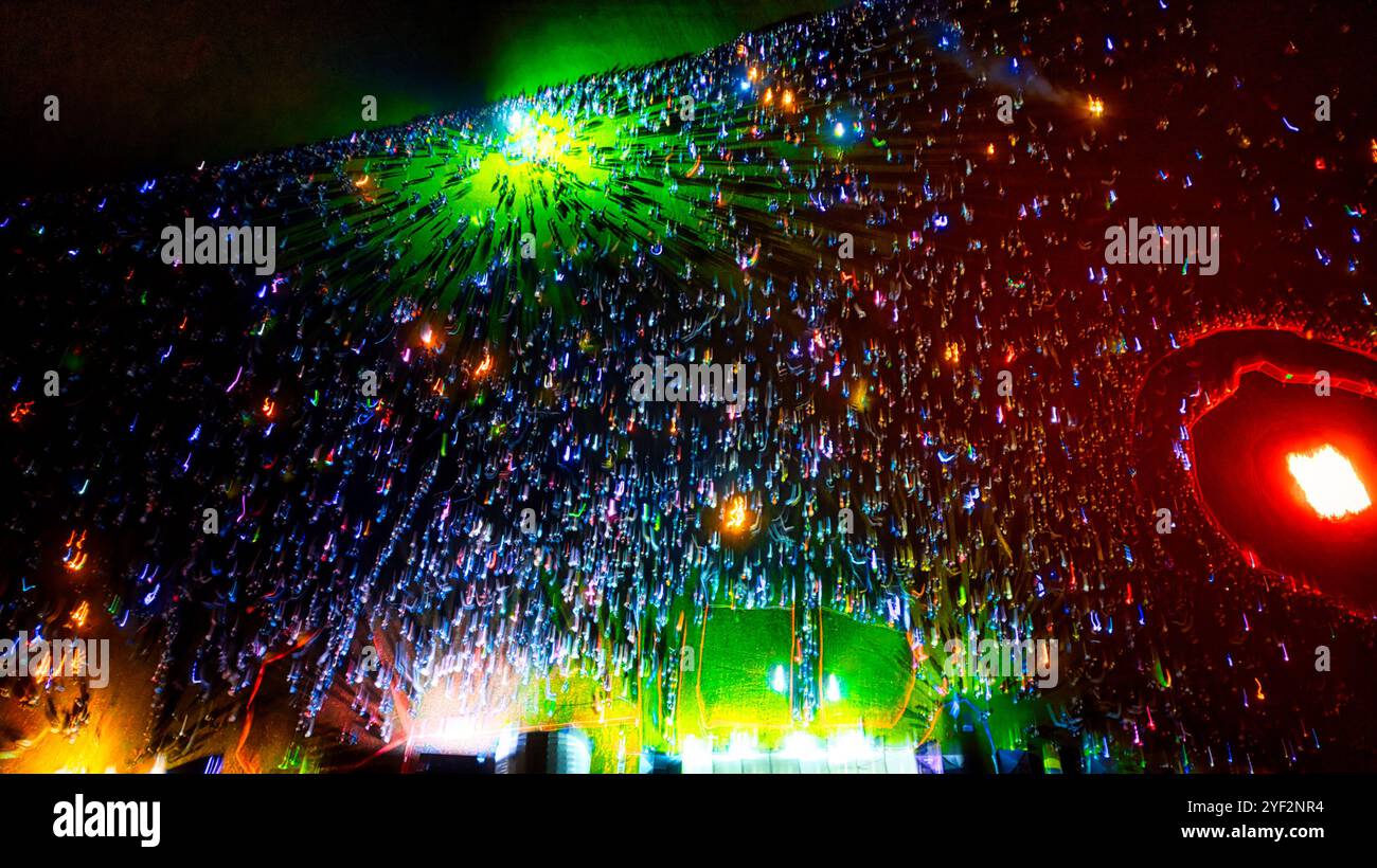 Un'ampia folla di persone tiene in mano delle levette luminose che creano strisce di luce colorate su uno sfondo scuro. Le luci sono prevalentemente blu, verdi, A. Foto Stock