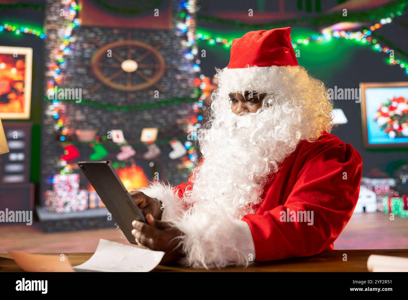 Babbo Natale naviga sul Web sul suo gadget tablet e controlla gli elenchi dei regali e le posizioni per la consegna sulla mappa del mondo. Cabina al Polo Nord piena di luci natalizie e magia, preparativi per le vacanze. Foto Stock