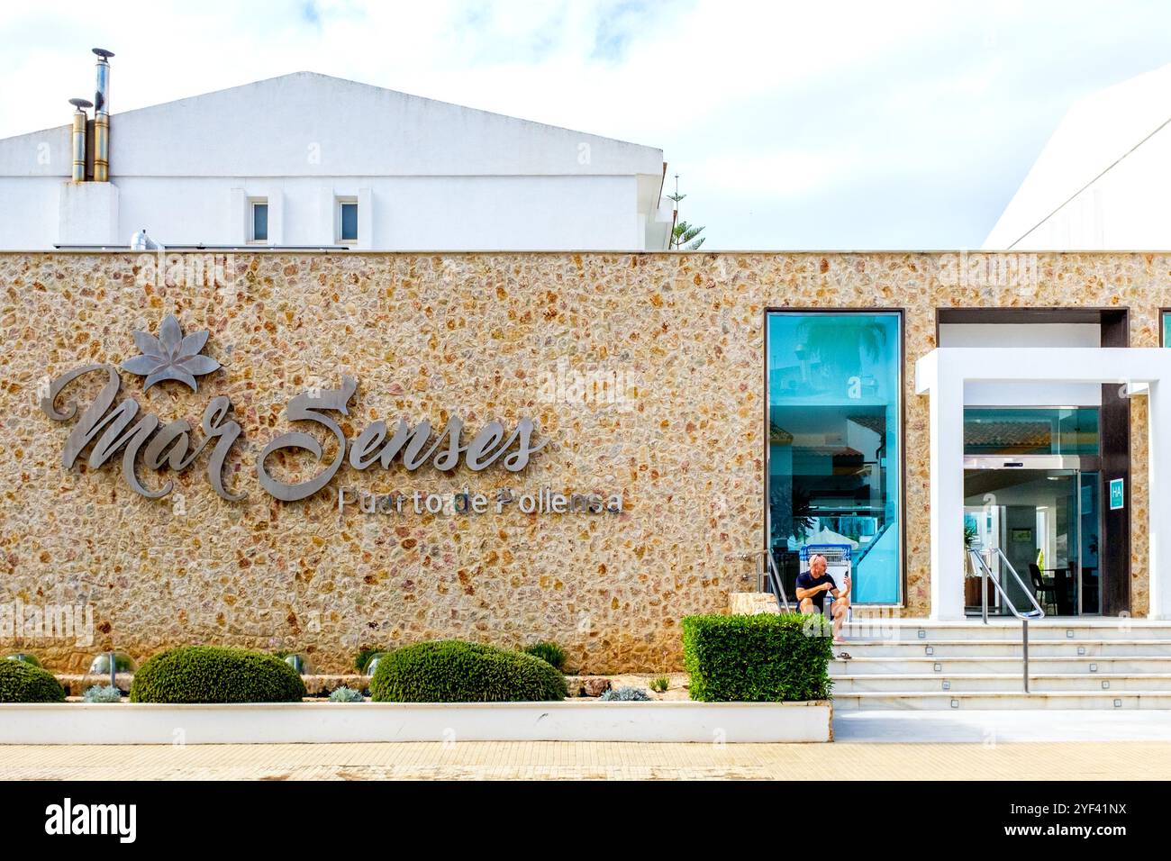 La facciata anteriore del MarSenses Puerto Pollensa Hotel and Spa a 4 stelle con una persona seduta su un gradino vicino alla porta. Foto Stock