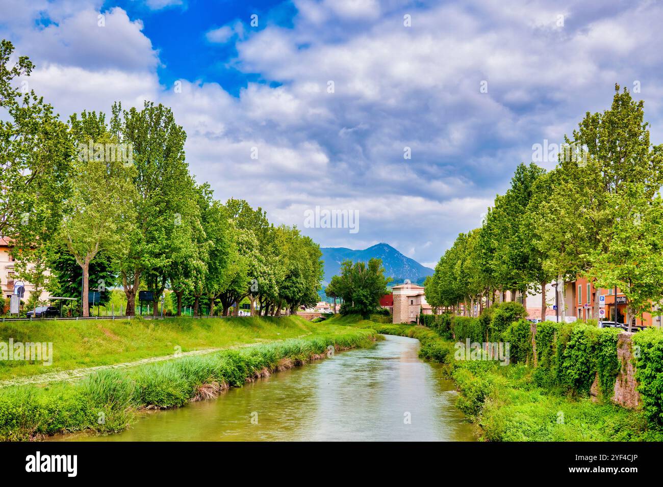Il fiume Topino scorre attraverso Foligno, in Italia, circondato da alberi verdi e da uno sfondo montuoso. Foto Stock