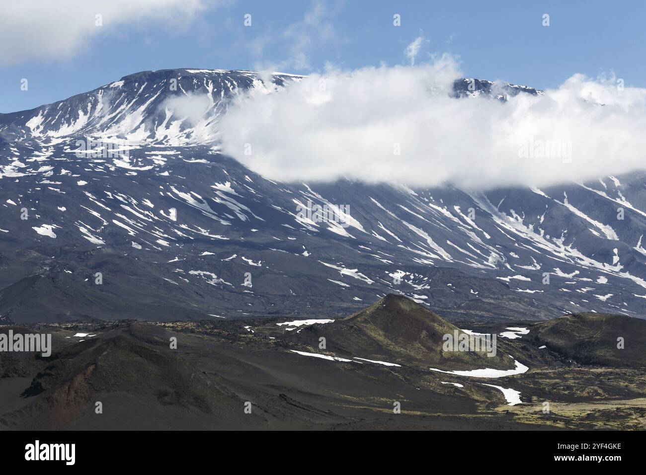 Paesaggio vulcanico della penisola di Kamchatka: Splendida vista estiva del cono del vulcano attivo Plosky Tolbachik e delle nuvole che nascondono parzialmente la cima del vol Foto Stock