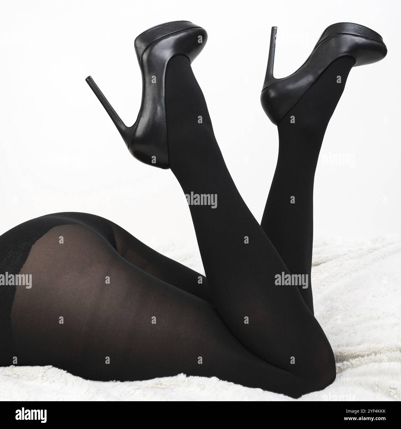 Donna vestita con collant neri e scarpe con tacco alto, è adagiata sul davanti con le gambe piegate in ginocchio e rialzate con il tacco. Vista rifilata di fe non riconoscibile Foto Stock