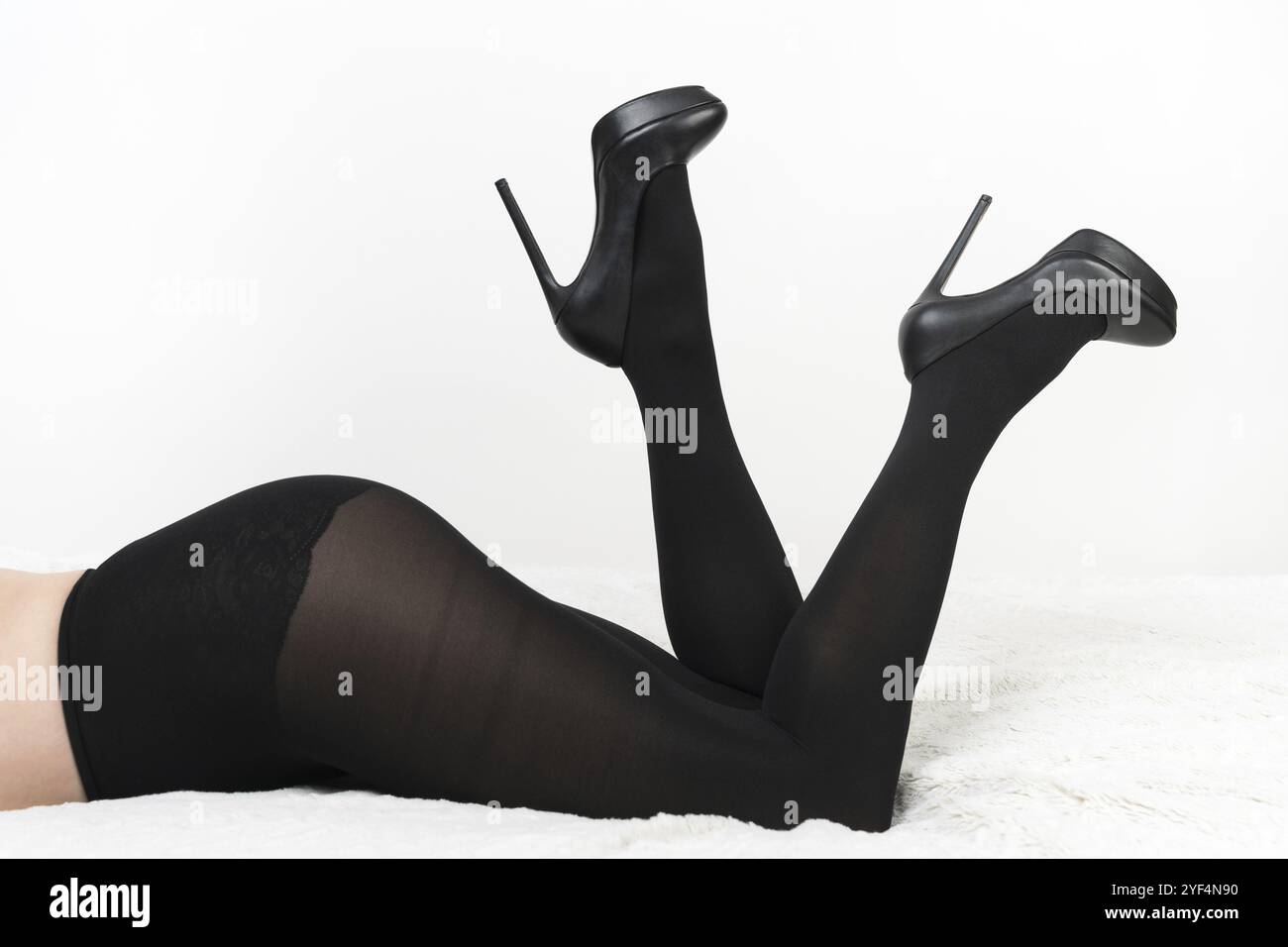 Vista rifilata della femmina con collant neri e scarpe con tacco alto sdraiate sul davanti con le gambe piegate in ginocchia e sollevate con i tacchi. Donna irriconoscibile o Foto Stock