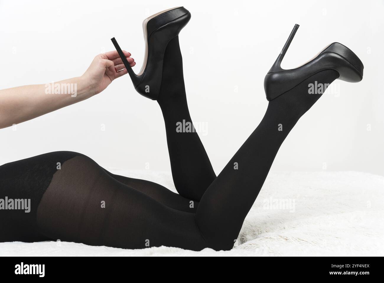 Donna vestita con collant neri e scarpe con tacco alto si trova sul davanti con le gambe piegate in ginocchio e rialzate con i tacchi. Una mano che tiene le scarpe sul tallone. CR Foto Stock