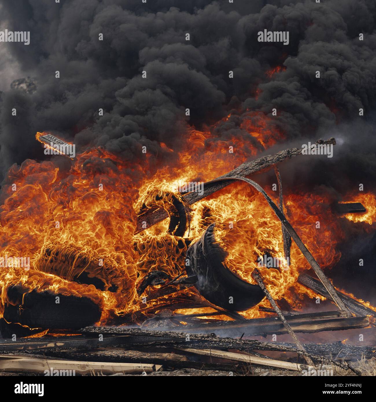 Ruote di automobili in fiamme, fiamma forte del fuoco rosso e nuvole di fumi neri nel cielo. Messa a fuoco selettiva, sfocatura dovuta al fuoco intenso Foto Stock