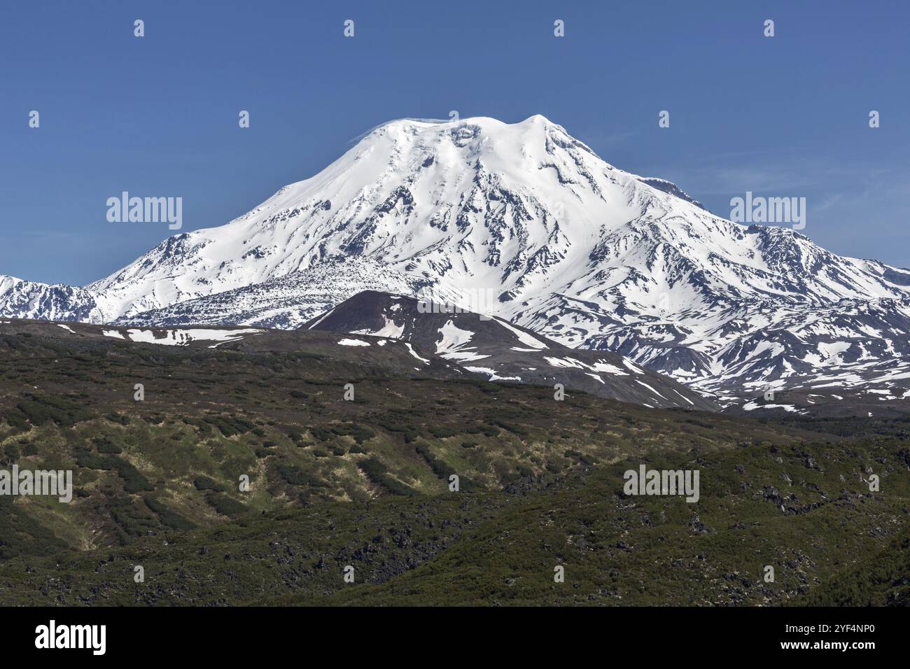 Vista panoramica delle montagne della penisola di Kamchatka: Vista panoramica estiva del cono innevato del vulcano attivo Ichinsky nelle giornate limpide e soleggiate con cielo blu. UE Foto Stock