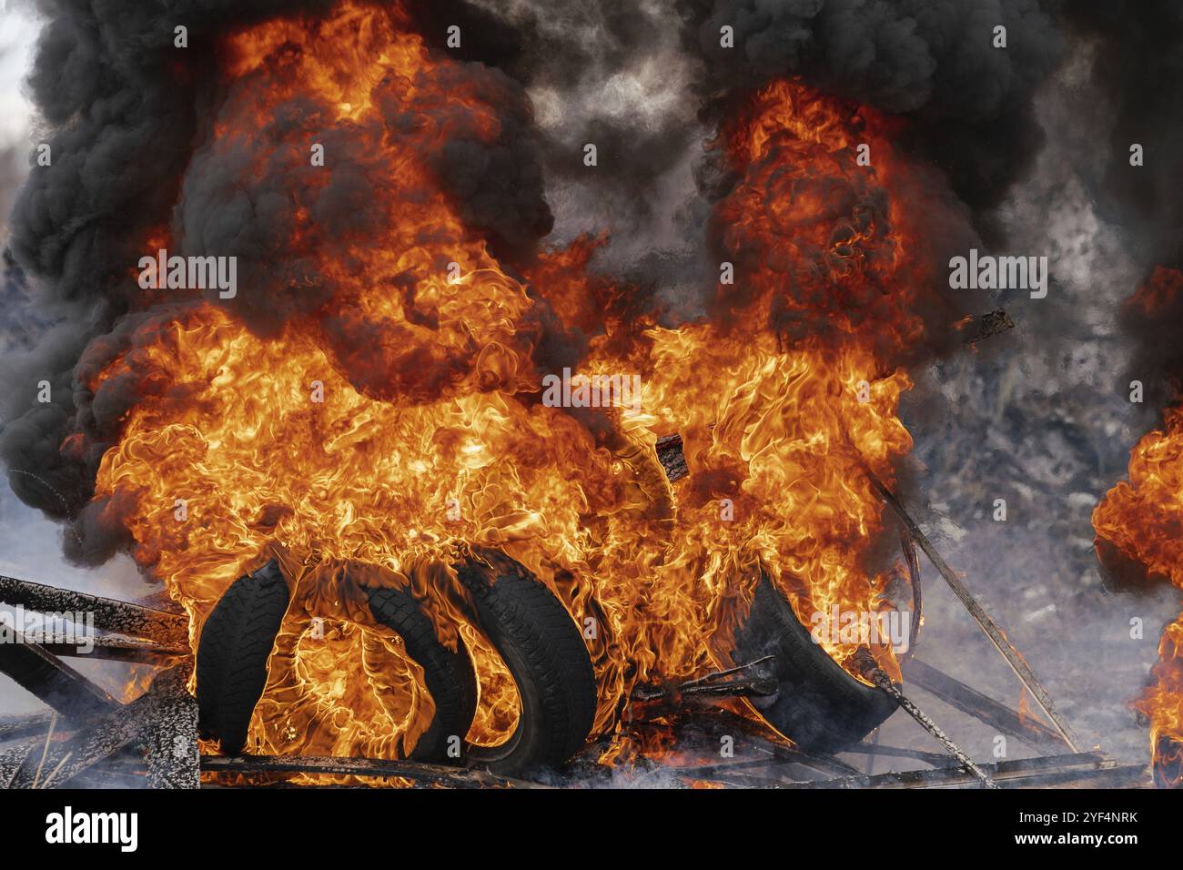 Pneumatici per automobili in fiamme, fiamme forti di fuoco rosso e nuvole di fumo nero nel cielo. Messa a fuoco selettiva, sfocatura dovuta al fuoco intenso Foto Stock