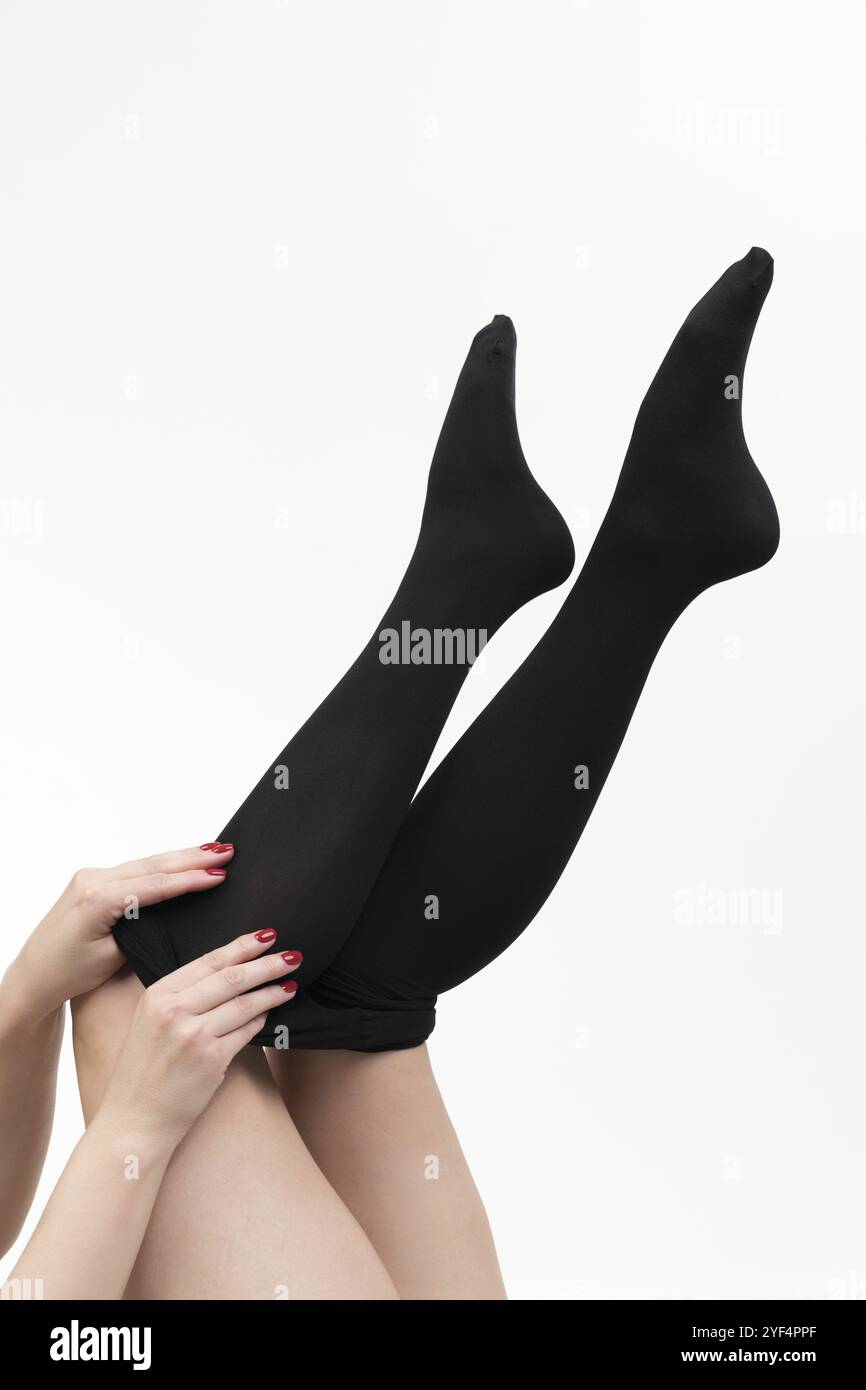 Vista ravvicinata delle mani femminili che indossano il collant nero. Vista rifilata delle gambe irriconoscibili della donna su sfondo bianco. Vista laterale, ripresa in studio. Parte di Foto Stock