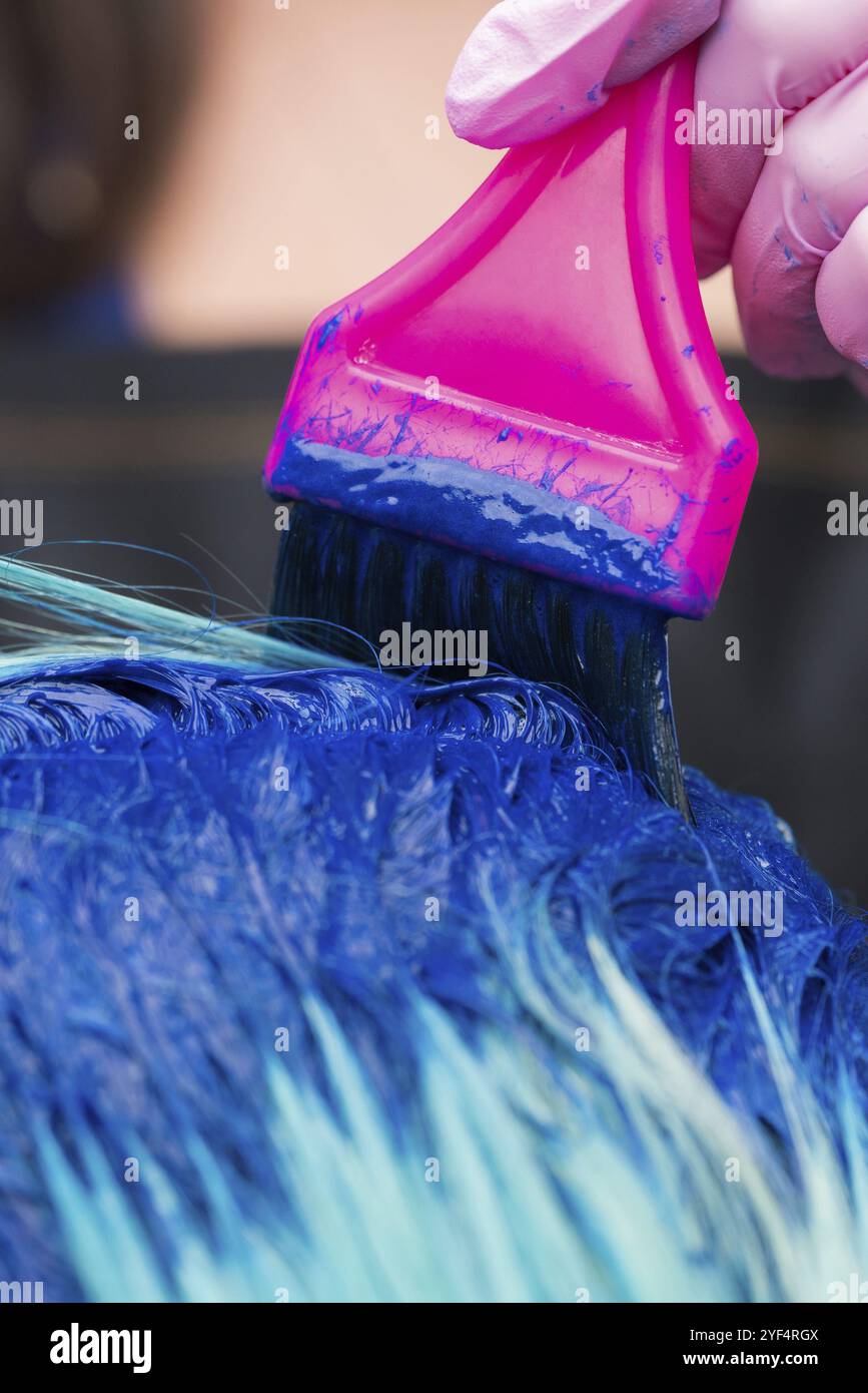 Parrucchiere in guanto protettivo con spazzola magenta mentre si applica vernice blu al colore smeraldo dei capelli, durante il processo di tintura dei capelli in colore elegante a. Foto Stock