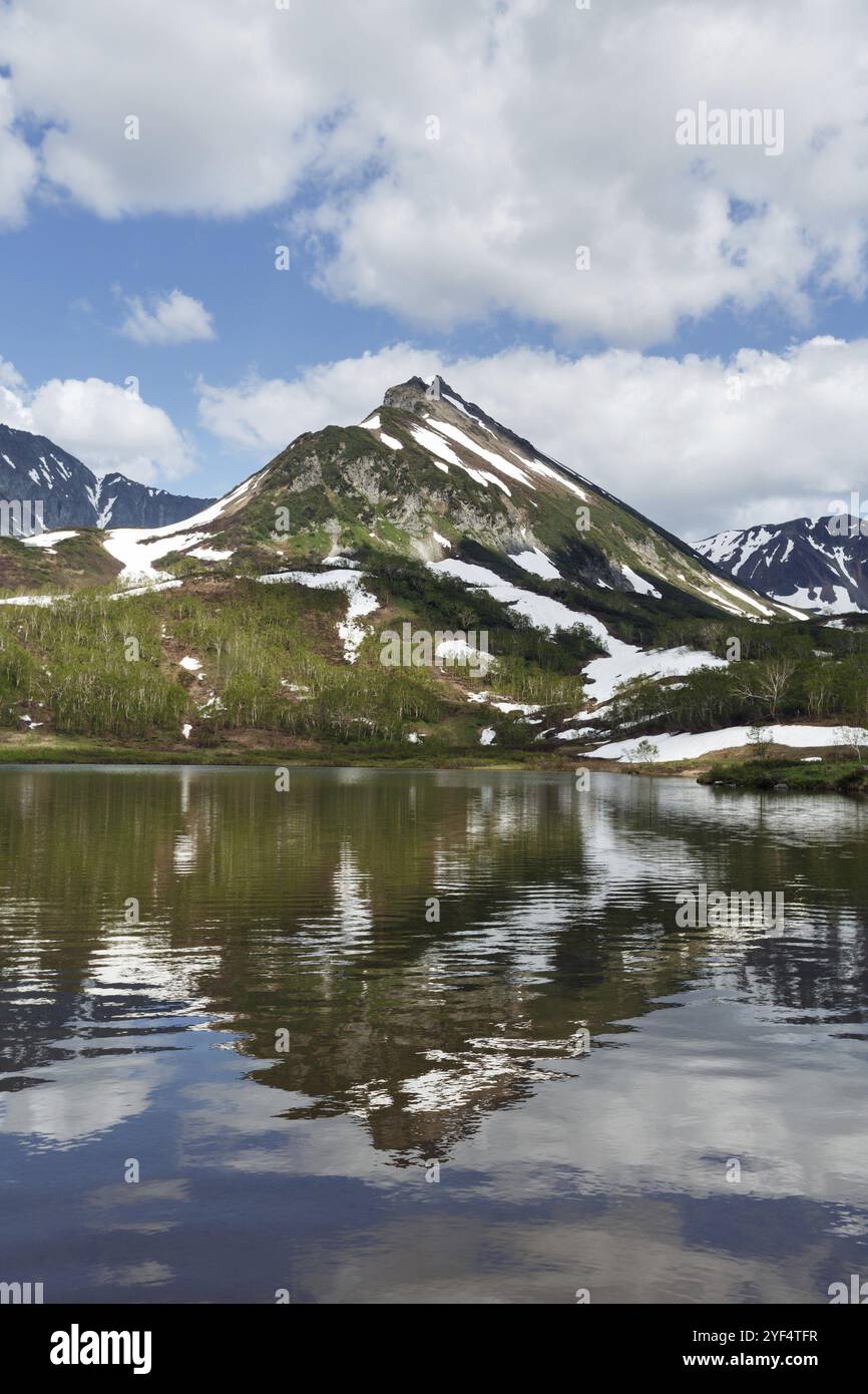 Splendido paesaggio estivo della penisola di Kamchatka: Vista della catena montuosa Vachkazhets, il loro riflesso nel lago di montagna e nuvole nel cielo blu al sole Foto Stock