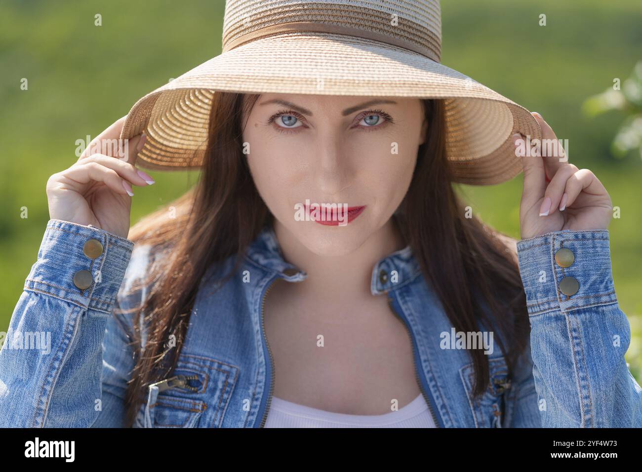 Ritratto di una donna con occhi grigi che guarda la fotocamera. Hipster femminile in piedi su sfondo naturale verde sfocato della foresta. Vista frontale dell'autentica bru Foto Stock