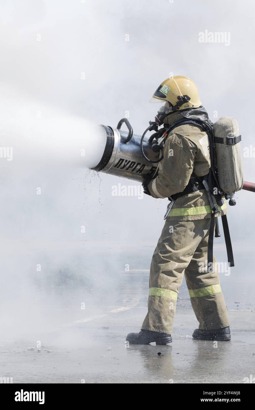 Un pompiere estingue l'incendio dalla manichetta antincendio, utilizzando un fusto di schiuma d'acqua antincendio con schiuma aria-meccanica. Festa dei vigili del fuoco. Foto Stock