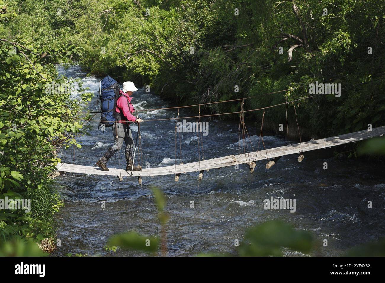 PENISOLA DI KAMCHATKA, RUSSIA, 11 LUGLIO 2014: Escursione estiva sulla Kamchatka, giovane escursionista con zaino dietro le spalle che attraversa il fiume di montagna Foto Stock