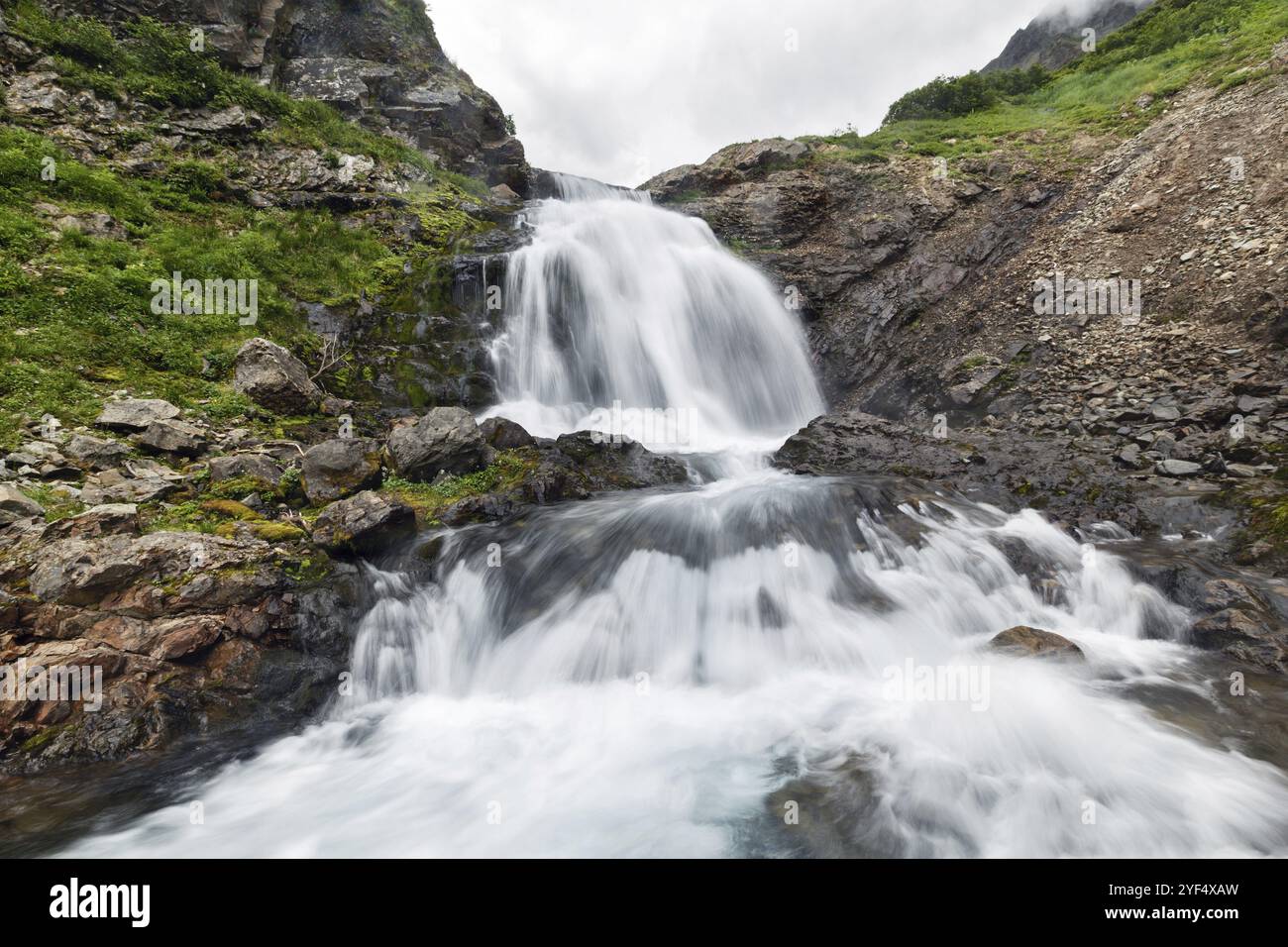Paesaggio montano estivo della penisola di Kamchatka: Splendida vista della cascata di acqua burrasca che scorre nella cascata della catena montuosa Vachkazhets Foto Stock