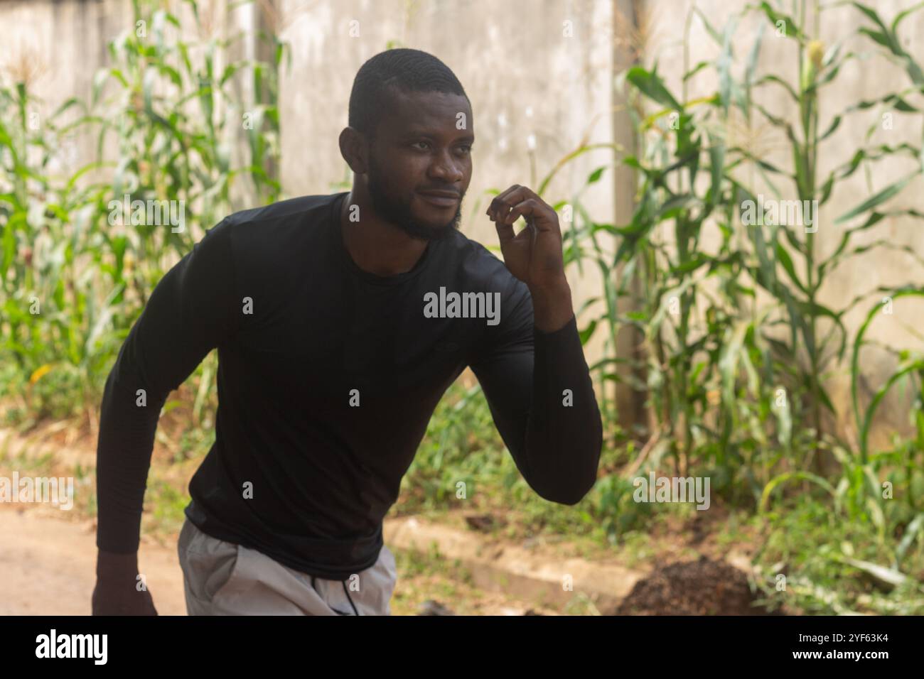 un giovane atletico adulto vestito con una camicia casual sul retro che si esercita e si tiene all'ombra degli alberi in una giornata calda Foto Stock