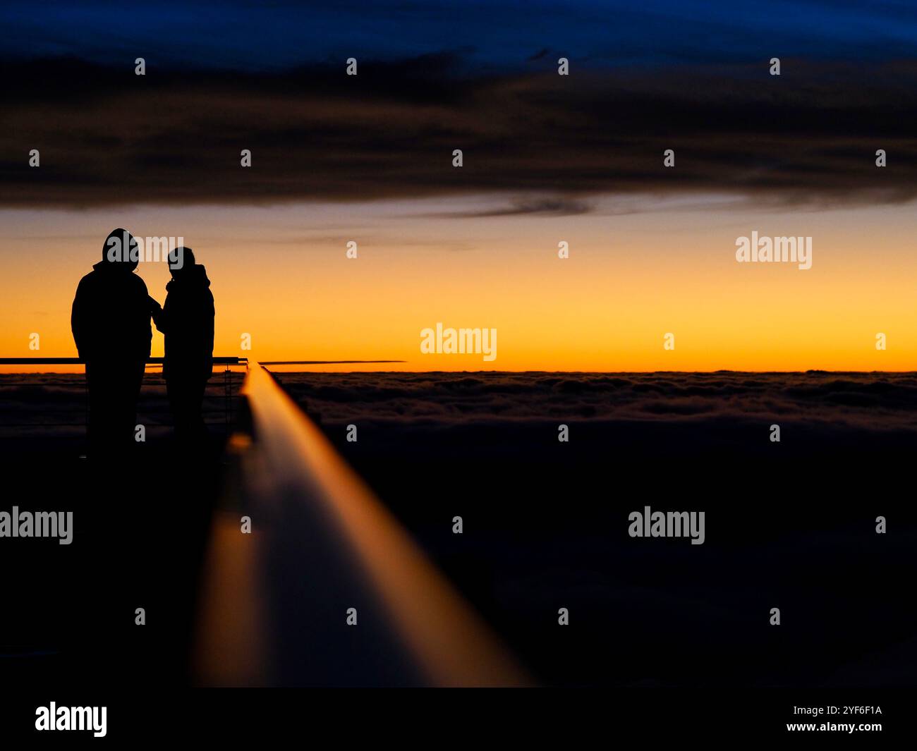 Due persone si stagliano come silhouette contro un cielo al tramonto vividamente dipinto, le loro figure trasmettono un senso di compagnia, bellezza e lo splendore di na Foto Stock