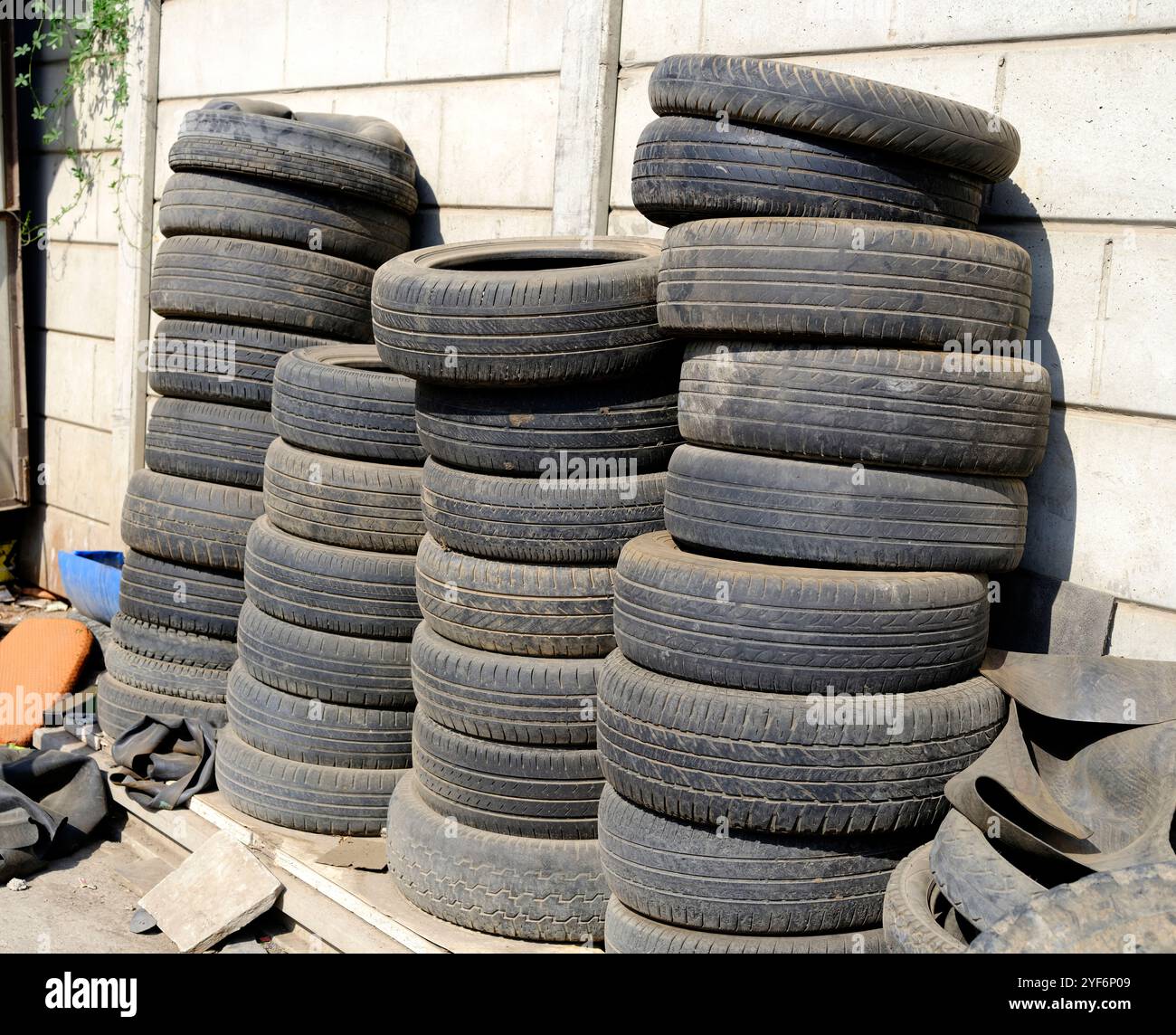 Un mucchio di pneumatici vecchi e usati impilati contro un muro di cemento all'esterno di un garage. Foto Stock