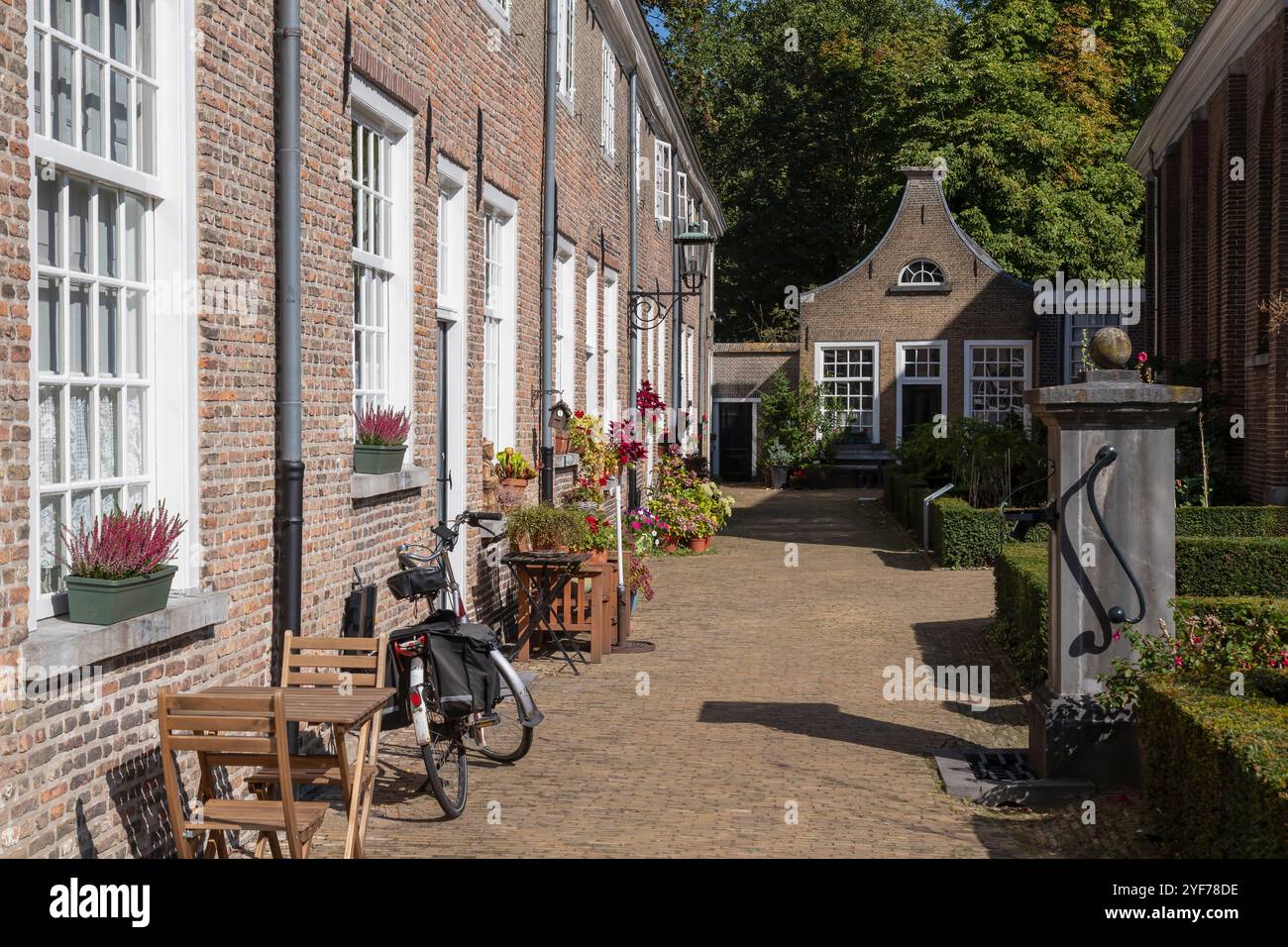 Beghinaggio medievale nel centro di Breda con piccole case storiche decorate con piante da giardino e una vecchia pompa dell'acqua in primo piano. Foto Stock