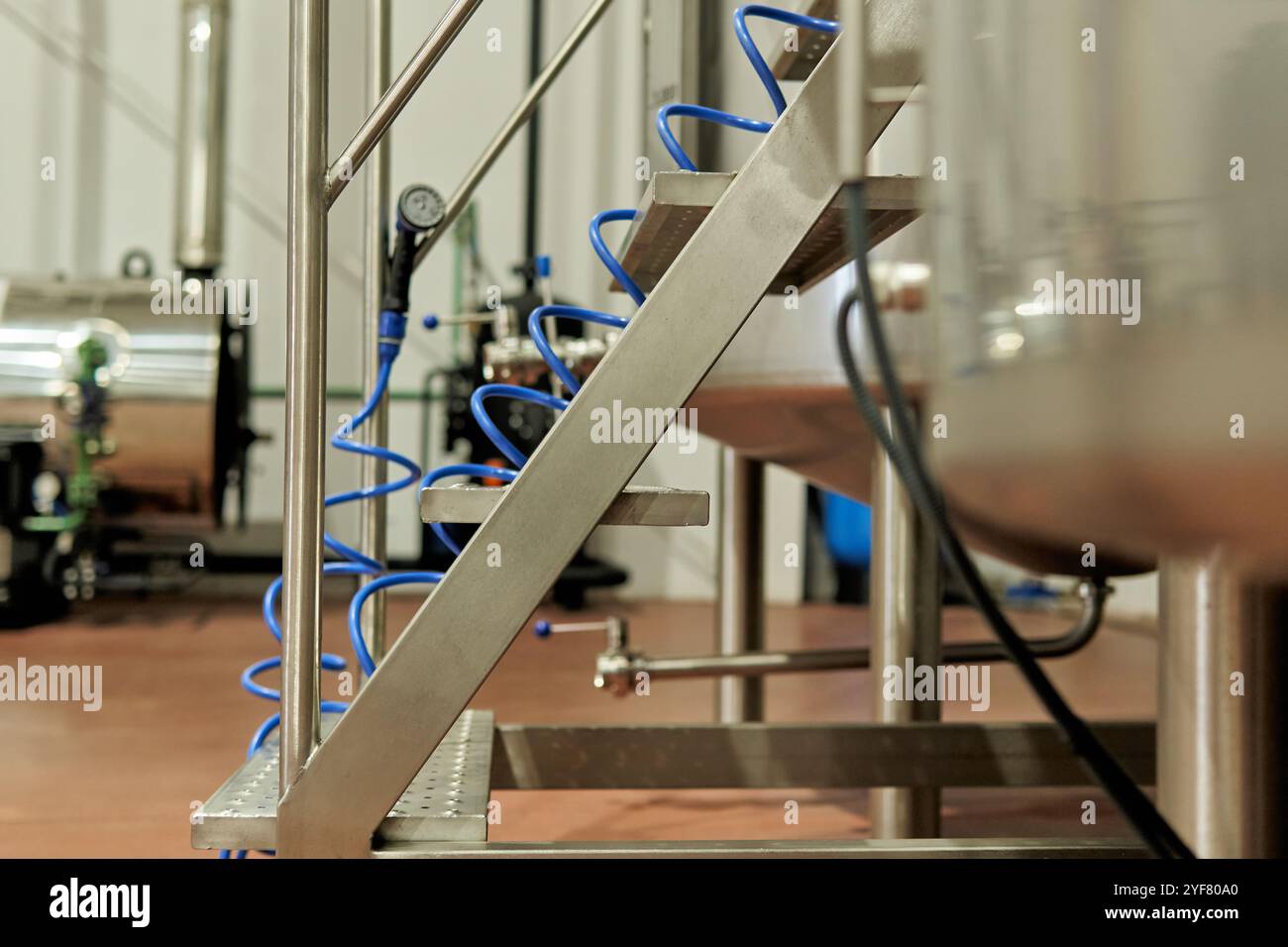 Scala industriale in acciaio inox con tubo flessibile a spirale blu nello stabilimento di produzione della birra Foto Stock