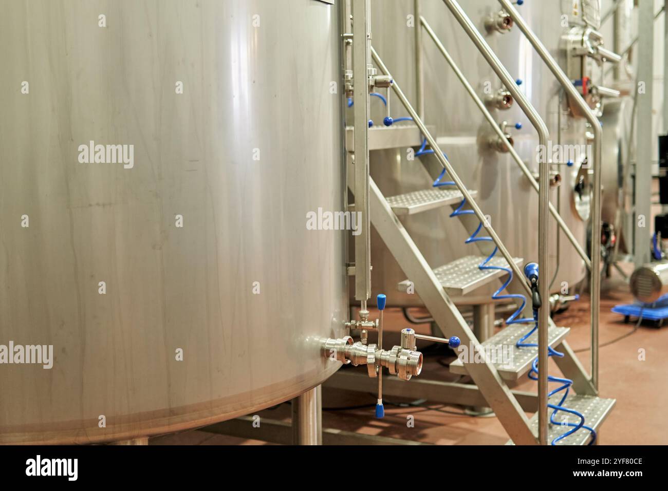 Scala industriale in acciaio inox con tubi blu avvolti in una fabbrica di birra Foto Stock