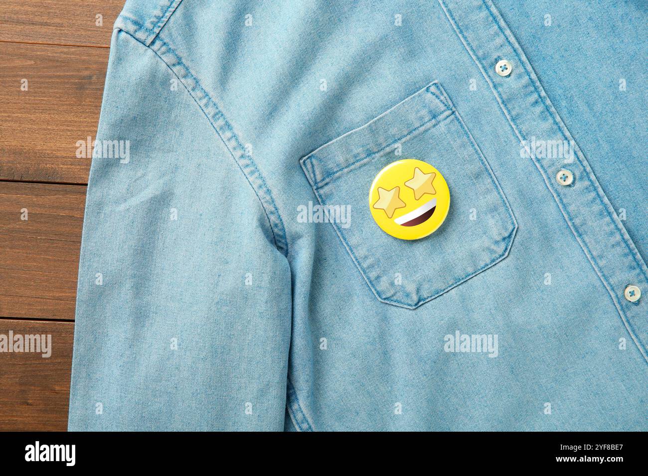 Badge con il volto a stella attaccato alla tasca della camicia in denim su sfondo in legno, vista dall'alto Foto Stock
