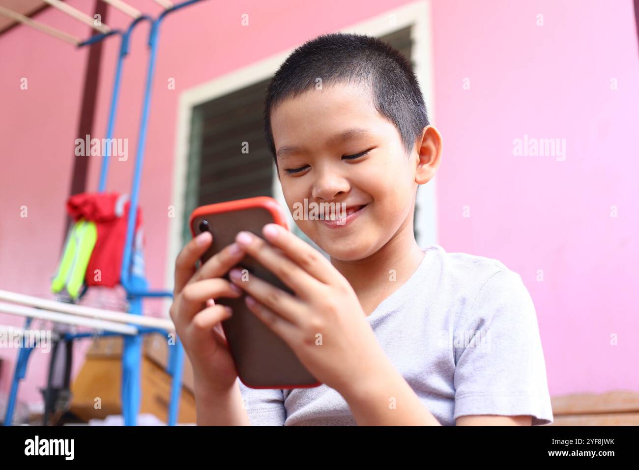 Un ragazzo felice sorride mentre guarda il suo smartphone, godendosi il momento all'aperto. Lo sfondo vibrante aggiunge un'atmosfera gioiosa e giocosa. Foto Stock