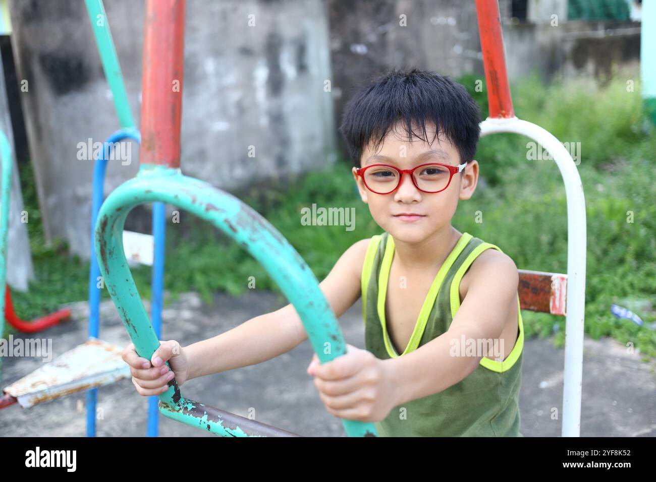 Un bambino gioioso con gli occhiali rossi gioca in un parco giochi colorato, irradiando felicità e innocenza. L'ambiente all'aperto cattura l'essenza dell'infanzia Foto Stock