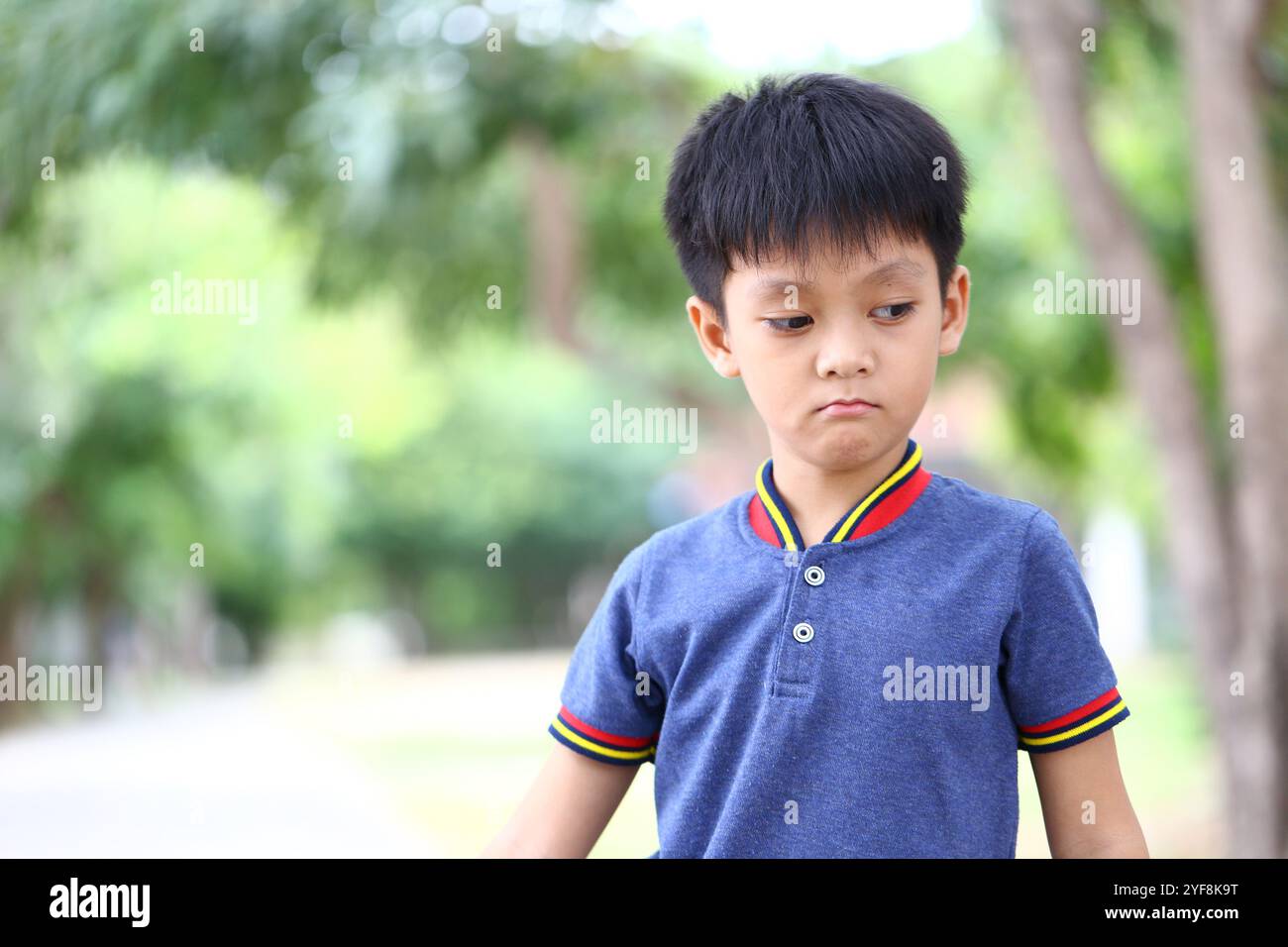 Un ragazzo dall'espressione triste si erge all'aperto, indossando una camicia blu. Il suo comportamento premuroso cattura l'essenza delle emozioni dell'infanzia durante la Sum Foto Stock