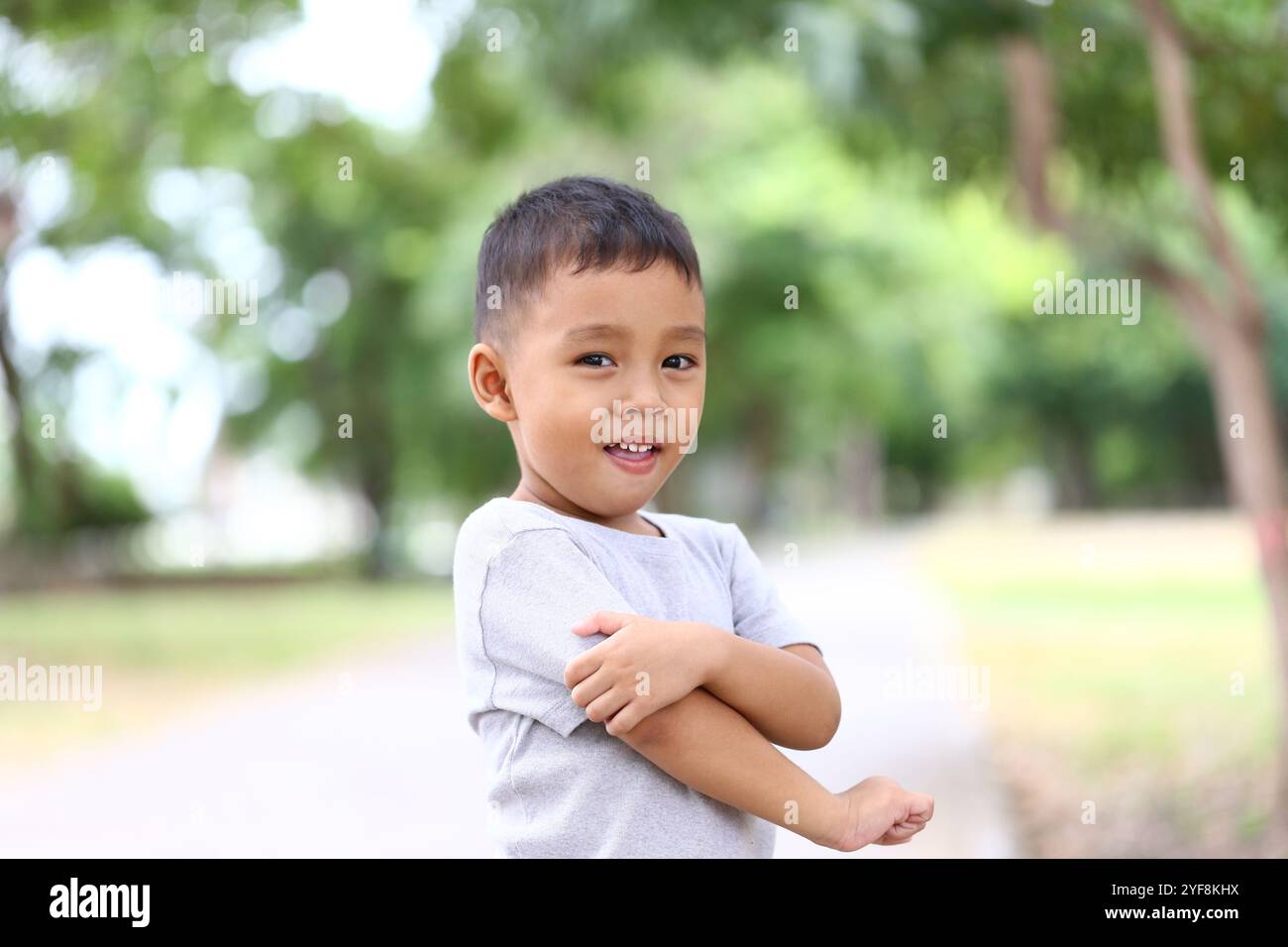 Un giovane gioioso sorridente mentre si trova in un parco all'aperto soleggiato. Questa coinvolgente immagine cattura l'innocenza e la giocosità dell'infanzia in a vi Foto Stock