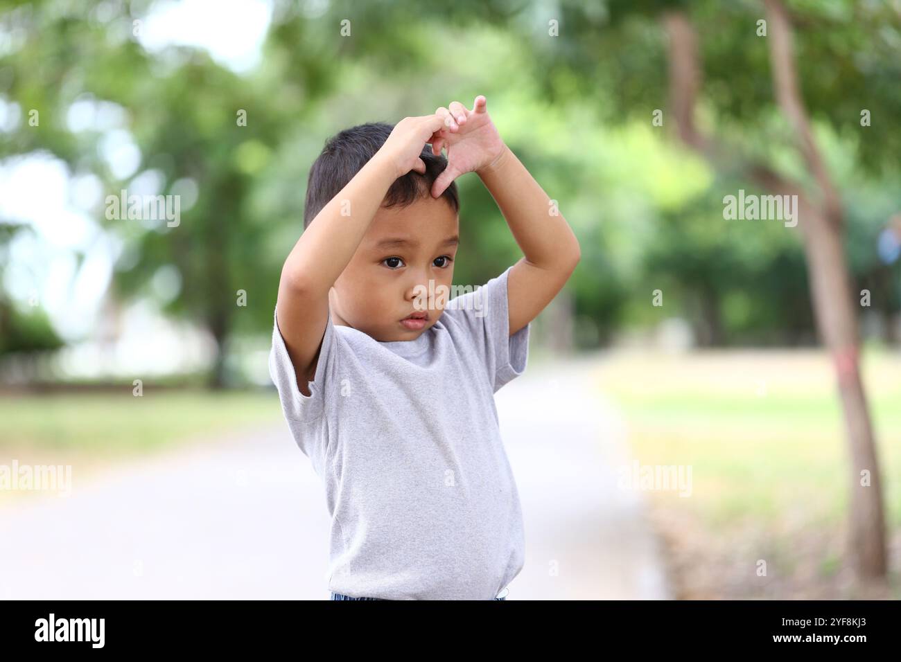 Un bambino premuroso si trova all'aperto in un parco tranquillo, a riflettere con un gesto espressivo. Questo affascinante momento cattura l'innocenza e le curiosi Foto Stock