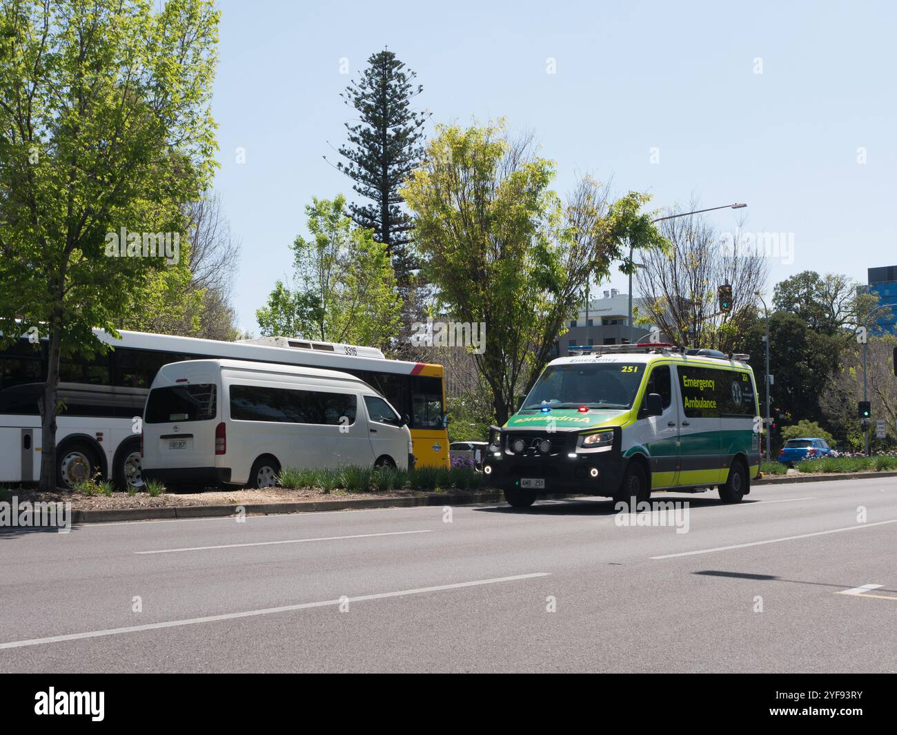 L'ambulanza viaggia lungo Hutt Street in una giornata luminosa e soleggiata ad Adelaide, Australia, con autobus e furgone sullo sfondo. Foto Stock