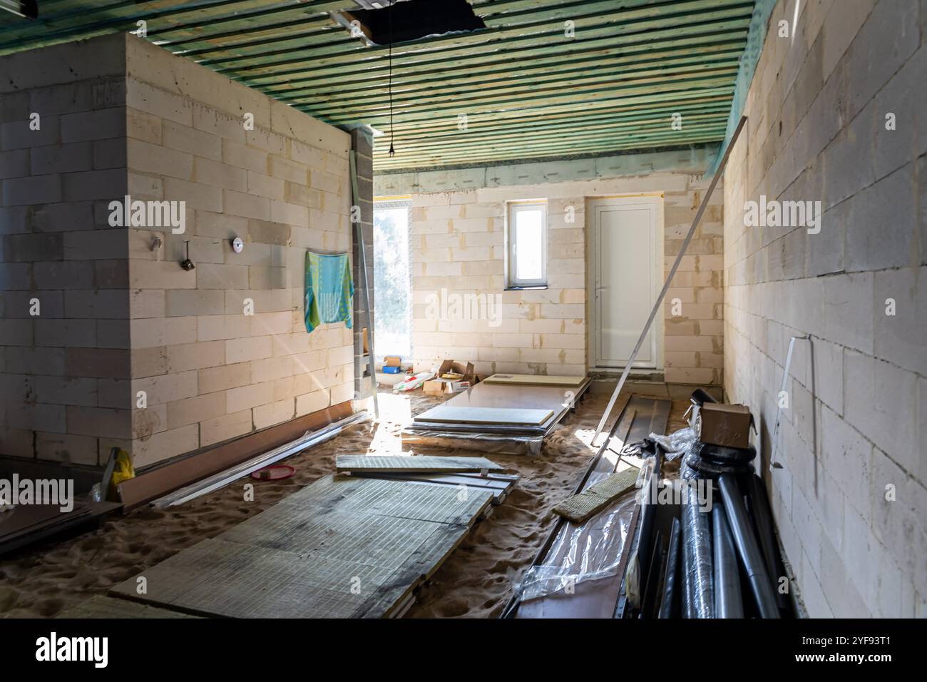 interni non rifiniti con pareti a blocchi esposte e materiali da costruzione sparsi su pavimento sabbioso sotto un soffitto a travi di legno Foto Stock