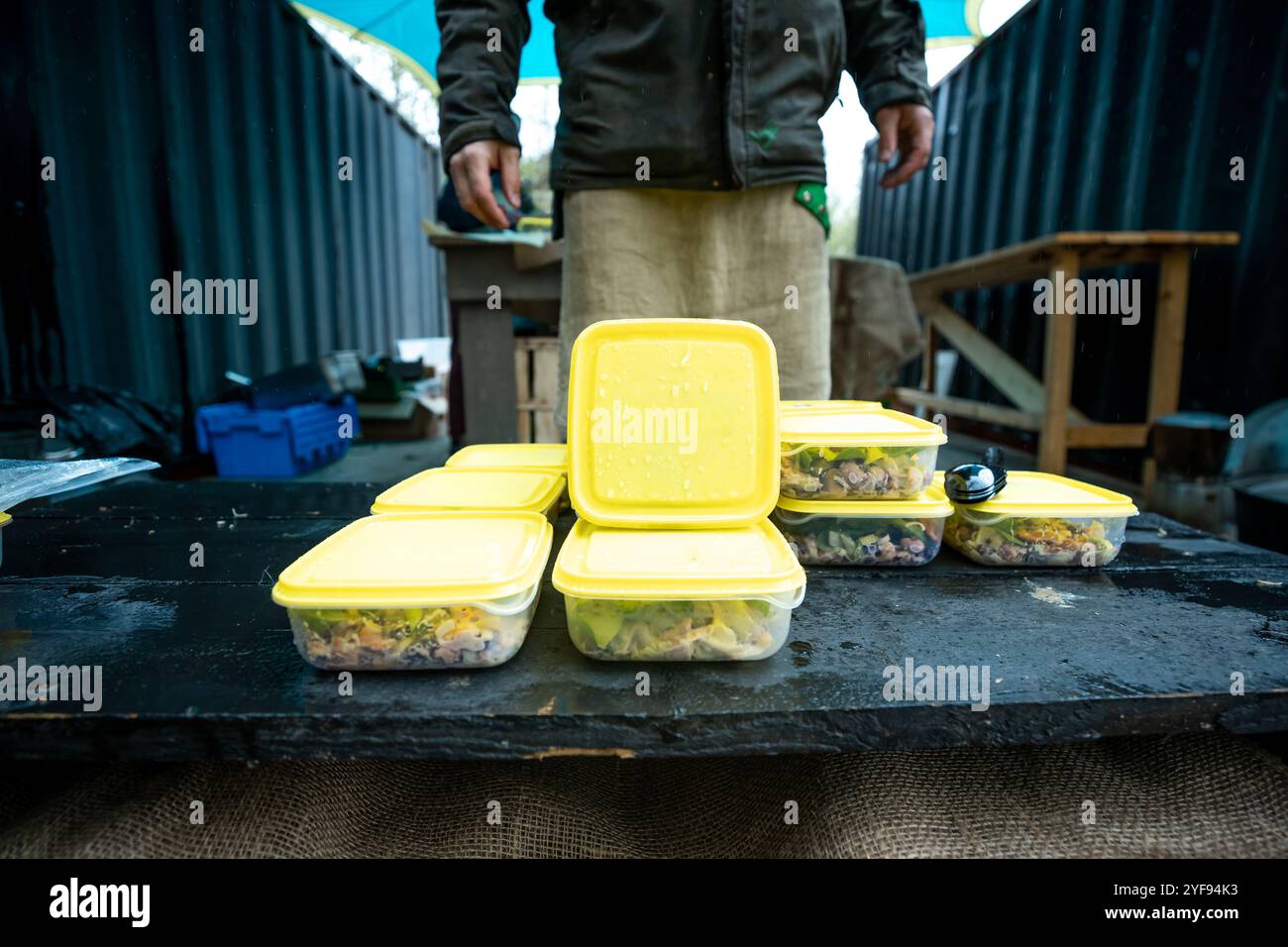 contenitori per pasti preparati allineati su un banco da lavoro rustico in un campeggio all'aperto con un telone blu sopra, che mostra la preparazione del cibo organizzato per il campeggio Foto Stock