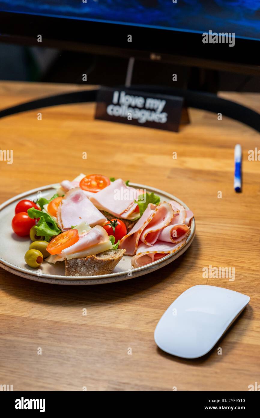 Moderna scrivania da ufficio con sandwich gourmet, espresso, smartphone e computer portatile per una giornata di lavoro produttiva Foto Stock
