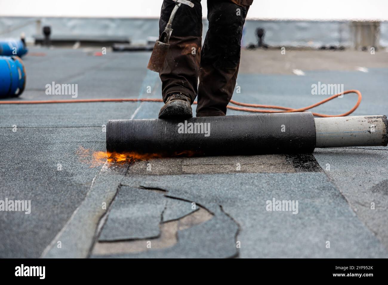 conciatetto professionale al lavoro per fissare la carta catrame arrotolata con una torcia a soffiaggio su un processo di installazione a tetto piatto Foto Stock