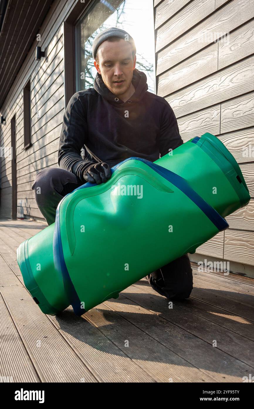 Preparazione per Water Adventures giovane uomo in piedi accanto a una tavola da SUP arrotolata su una piattaforma di legno Foto Stock