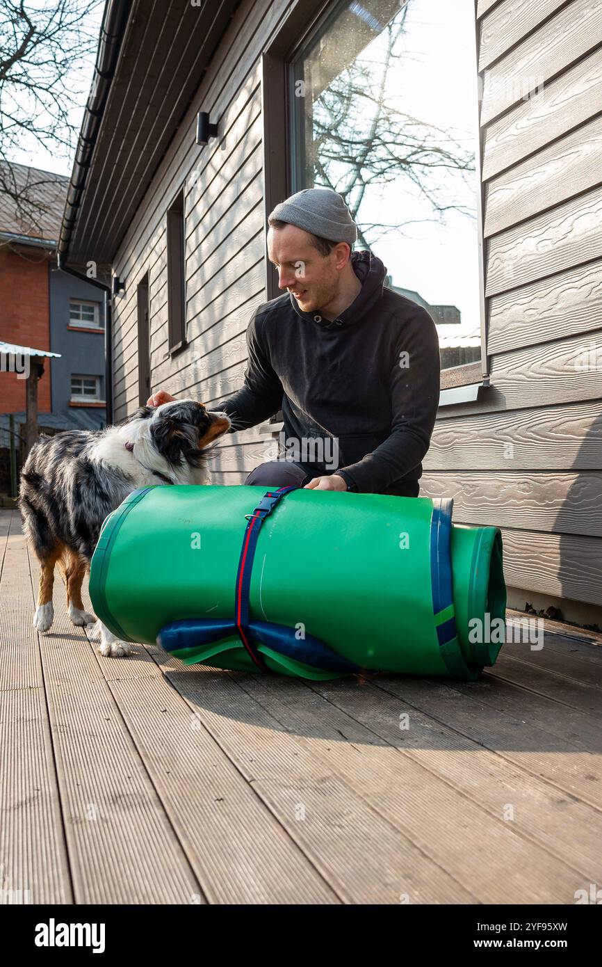 Preparazione per Water Adventures giovane uomo in piedi accanto a una tavola da SUP arrotolata su una piattaforma di legno Foto Stock