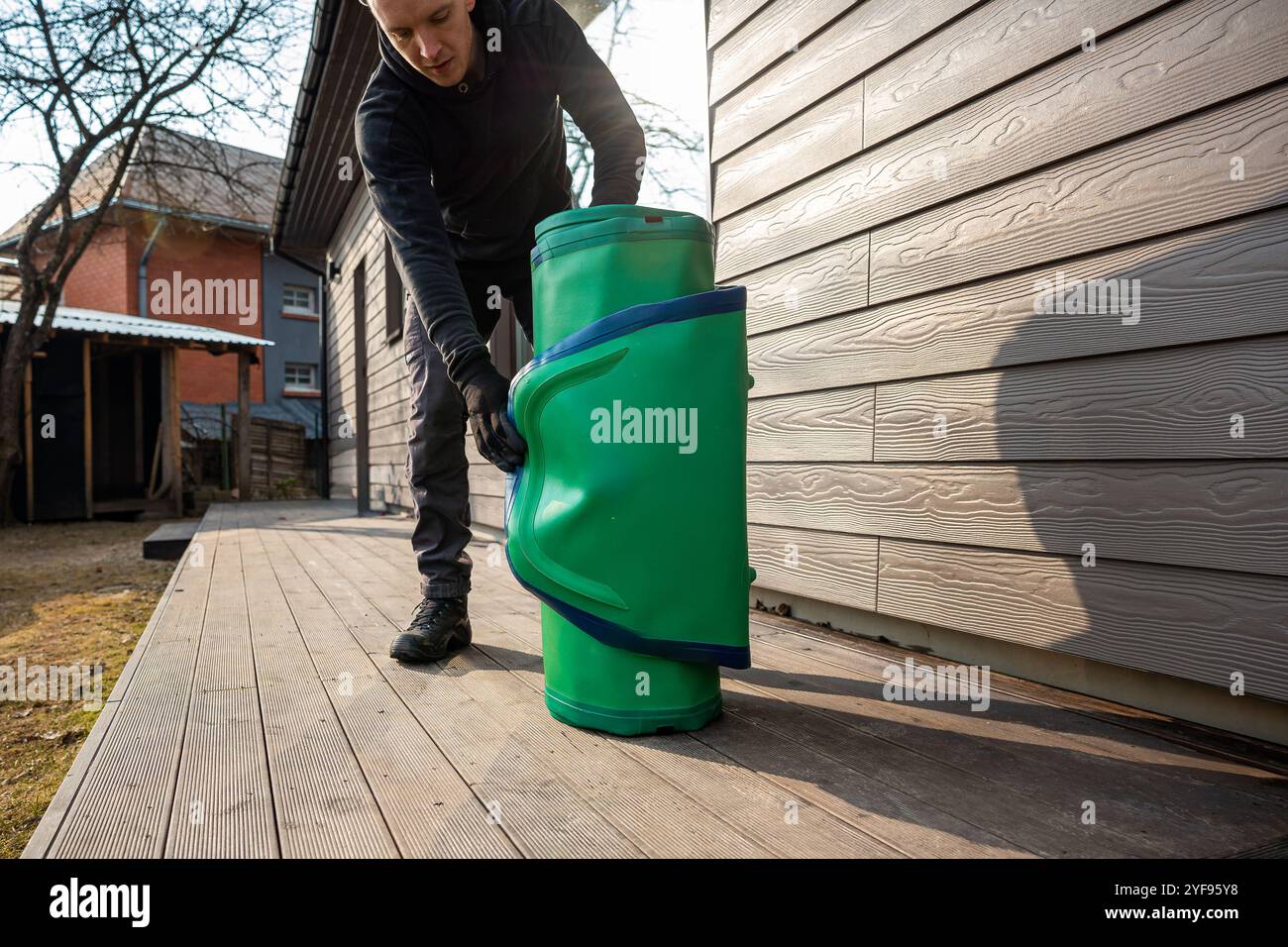 Preparazione per Water Adventures giovane uomo in piedi accanto a una tavola da SUP arrotolata su una piattaforma di legno Foto Stock