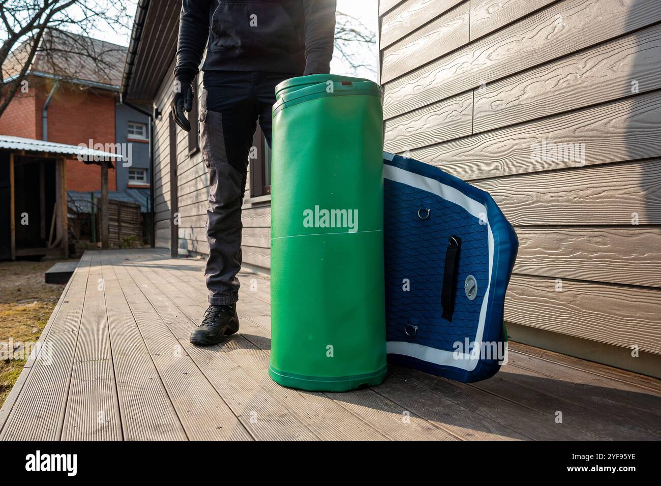 Preparazione per Water Adventures giovane uomo in piedi accanto a una tavola da SUP arrotolata su una piattaforma di legno Foto Stock
