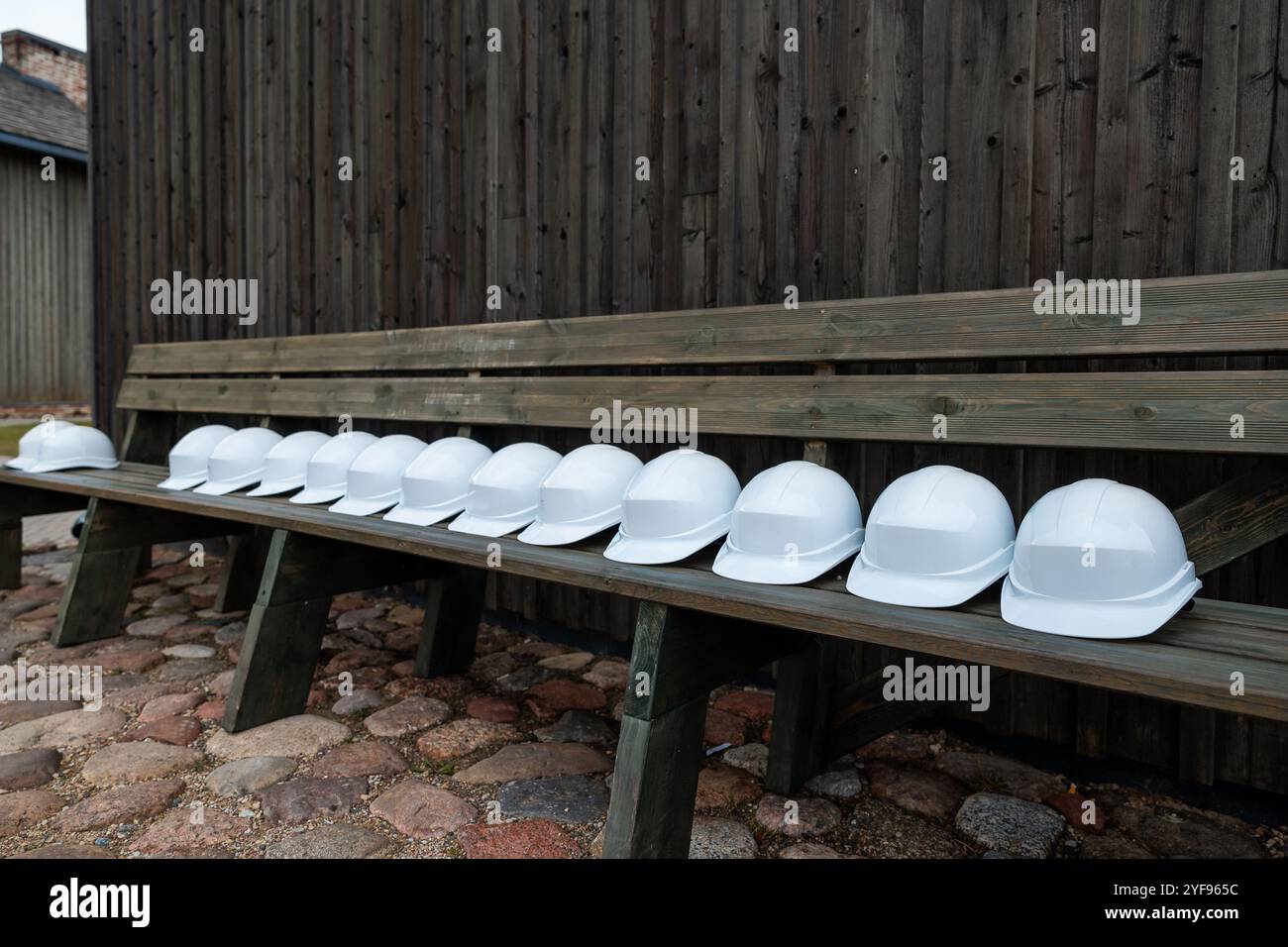 Fila di caschi di sicurezza bianchi allineati su un banco di legno su sfondo in legno scuro Foto Stock