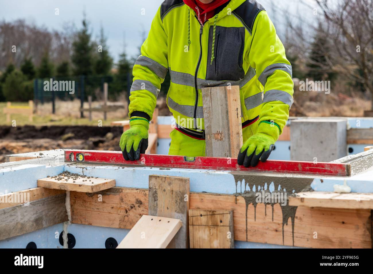 Operaio edile che utilizza la livella su forme di calcestruzzo isolate presso il cantiere edile Foto Stock