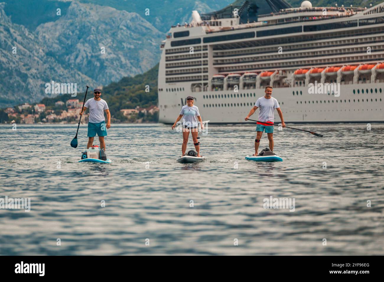tre pagaiatori in un'avventura panoramica di fronte a una maestosa nave da crociera con sfondo di montagna Foto Stock
