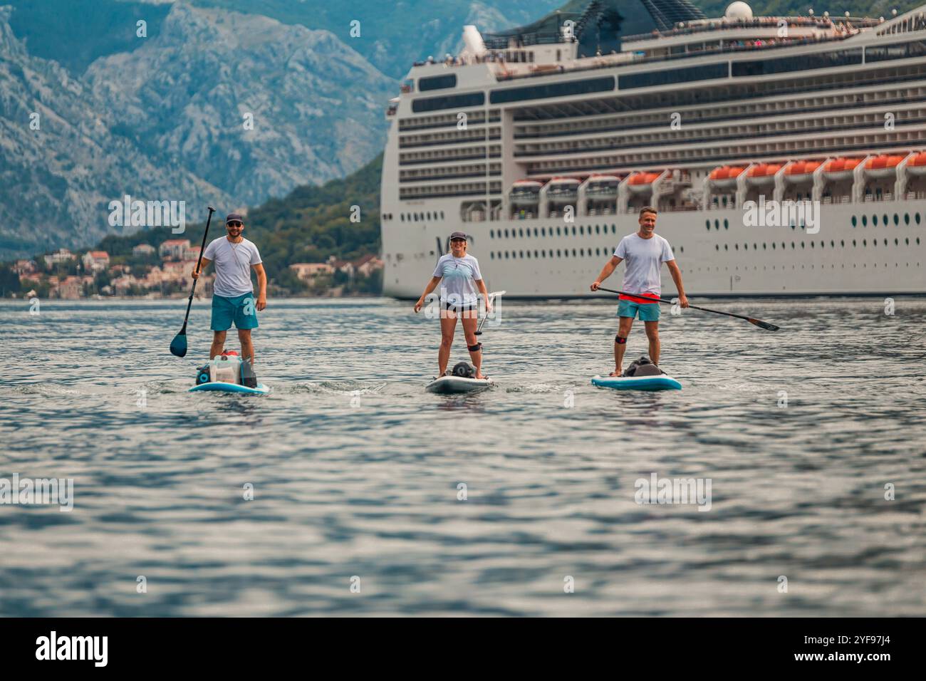 tre pagaiatori in un'avventura panoramica di fronte a una maestosa nave da crociera con sfondo di montagna Foto Stock