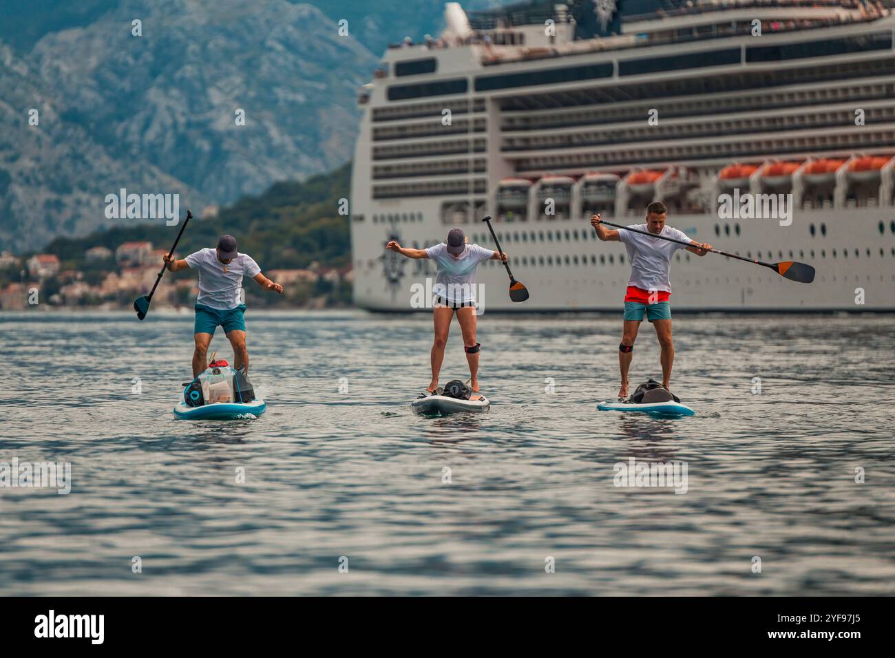tre pagaiatori in un'avventura panoramica di fronte a una maestosa nave da crociera con sfondo di montagna Foto Stock