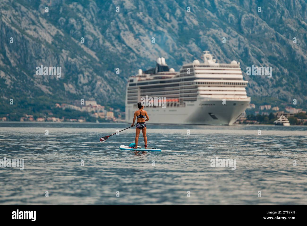 pagaia da solo di fronte a una torreggiante nave da crociera con uno splendido sfondo montuoso Foto Stock