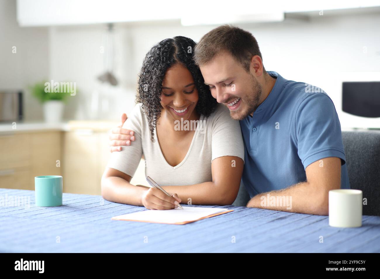 Felice coppia affettuosa che firma un contratto di carta nella cucina di casa Foto Stock
